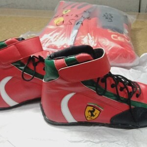 May include: Red high-top sneakers with white accents and black laces. The sneakers feature green trim and a yellow emblem with a black horse. A red bag with a logo is in the background.