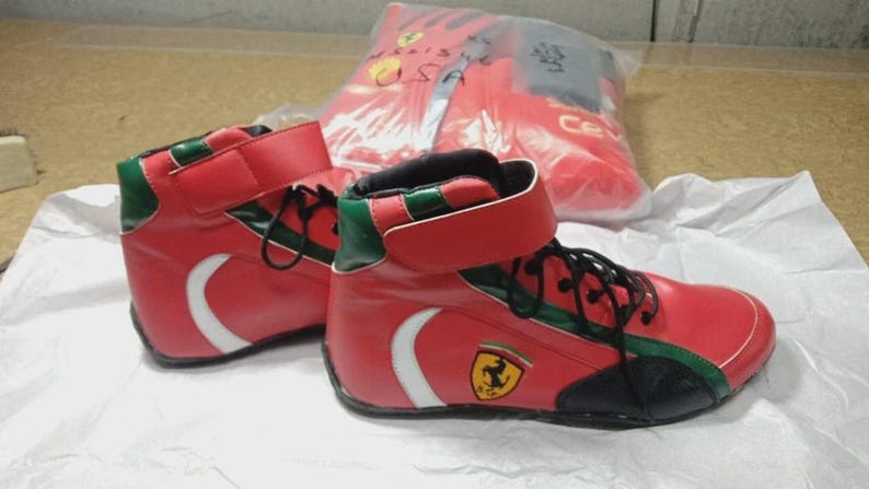 May include: Red high-top sneakers with white accents and black laces. The sneakers feature green trim and a yellow emblem with a black horse. A red bag with a logo is in the background.