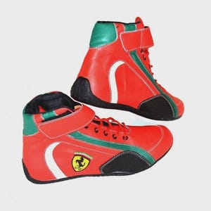 May include: Pair of red and green high-top sneakers with white accents and black soles. The sneakers feature a hook-and-loop strap and a small logo on the side. The shoes are designed for athletic activities.