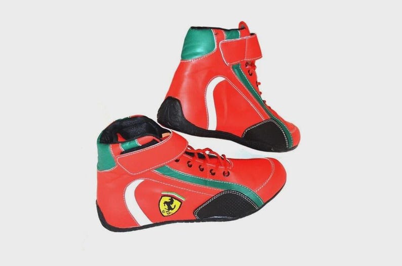 May include: Pair of red and green high-top sneakers with white accents and black soles. The sneakers feature a hook-and-loop strap and a small logo on the side. The shoes are designed for athletic activities.