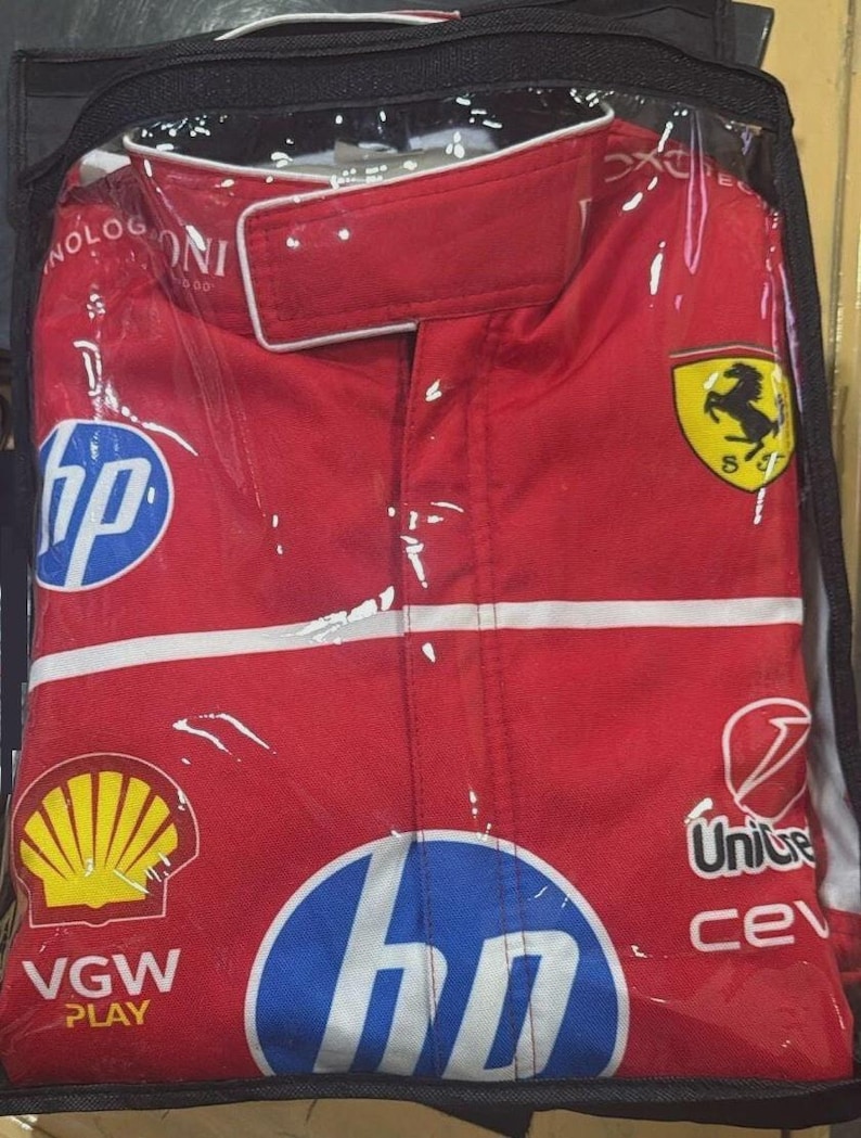 May include: Red racing suit with white accents, logos for HP, Shell, and Ferrari. The suit is enclosed in a clear plastic bag. The Ferrari logo features a black horse on a yellow shield.