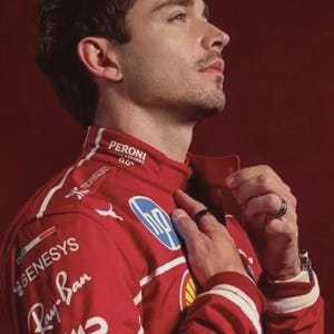 May include: A red racing jacket with sponsor logos, including Ray-Ban and Pirelli, is worn by a person. The jacket has white accents and a high collar. The background is a solid red.