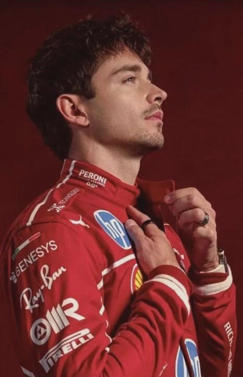 May include: A red racing jacket with sponsor logos, including Ray-Ban and Pirelli, is worn by a person. The jacket has white accents and a high collar. The background is a solid red.