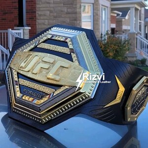 May include: A gold and black UFC championship belt with the words "CHAMPION" and "MCMXCIII" on the front. The belt is made of leather and has a hexagonal design.