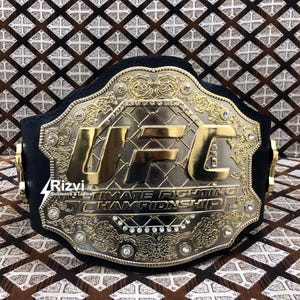 May include: A gold and black UFC championship belt with the words "Ultimate Fighting Championship" and "UFC" in gold lettering.