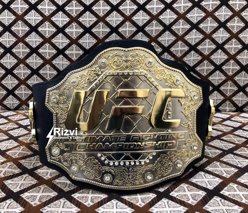 May include: A gold and black UFC championship belt with the words "Ultimate Fighting Championship" and "UFC" in gold lettering.