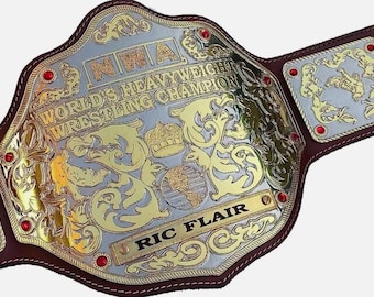 Può includere: Una cintura da campione di wrestling dei pesi massimi NWA World's in oro e argento con il nome "Ric Flair". La cintura ha un cinturino in pelle marrone ed è decorata con gioielli rossi e disegni ornati.