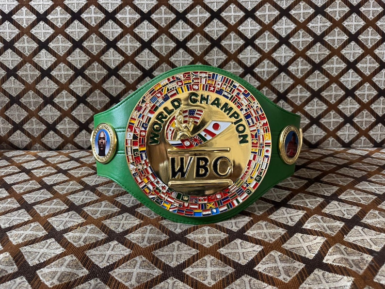 May include: A green and gold World Boxing Council (WBC) championship belt. The belt features a large central emblem with the words "WORLD CHAMPION" and "WBC". The belt is adorned with flags and portraits.