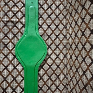 May include: A bright green leather belt with a wide, padded center section and a series of holes for adjustment. The belt is shown against a patterned brown and tan fabric background.