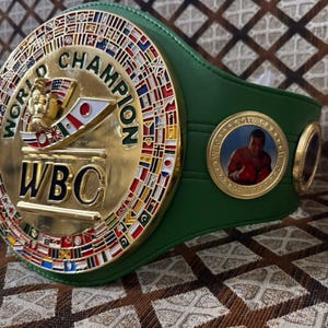 May include: A green and gold World Boxing Council (WBC) championship belt. The gold center features the words "World Champion" and "WBC", with flags around the perimeter. A circular emblem with a boxer is on the side.