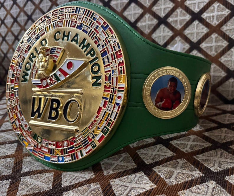 May include: A green and gold World Boxing Council (WBC) championship belt. The gold center features the words "World Champion" and "WBC", with flags around the perimeter. A circular emblem with a boxer is on the side.