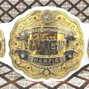 May include: A gold and silver wrestling championship belt with the text "INTERCONTINENTAL" and "IWGP CHAMPION". The belt has a white strap and is adorned with red and clear gemstones.