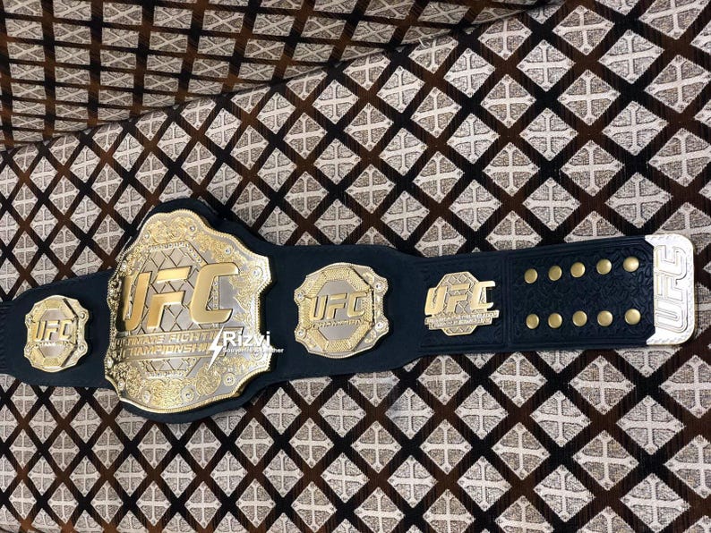 May include: A black leather UFC championship belt with gold accents and the UFC logo. The belt has multiple plates with the UFC logo and the words "Ultimate Fighting Championship".