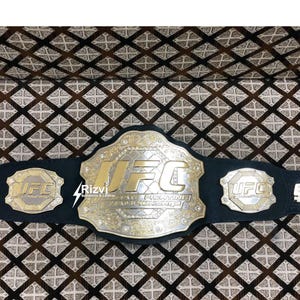 May include: A black leather UFC championship belt with gold accents and the words "UFC Ultimate Fighting Championship" on the front. The belt has three smaller plates with the UFC logo on each.