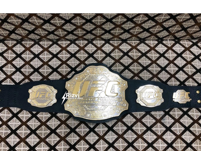 May include: A black leather UFC championship belt with gold accents and the words "UFC Ultimate Fighting Championship" on the front. The belt has three smaller plates with the UFC logo on each.