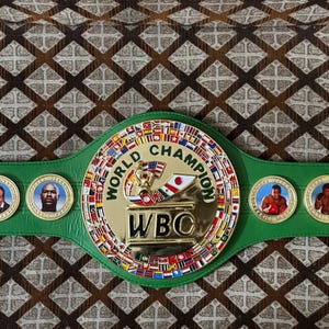 May include: A green and gold World Boxing Council (WBC) championship belt. The belt features a large central emblem with the words "World Champion" and "WBC". The belt has several medallions with portraits of boxers.