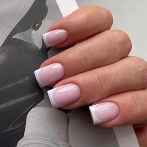 Op de afbeelding: Vierkant gevormde vingernagels met een klassiek Frans manicureontwerp. De nagels hebben een zachte, doorschijnende roze basiskleur met heldere, dekkende witte uiteinden, wat zorgt voor een verzorgde uitstraling met een glanzende afwerking.