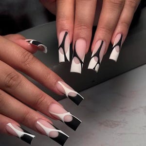 Puede incluir: Uñas artificiales largas de forma cuadrada con una base de color nude y complejos diseños de líneas abstractas en blanco y negro. Los patrones crean un contraste gráfico moderno en la superficie de cada uña, desde la cutícula hasta la punta.