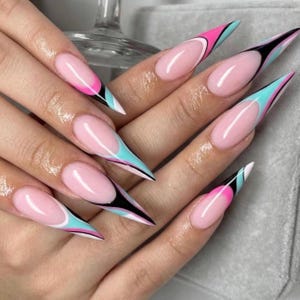 May include: A close-up of a hand displaying long, pointed acrylic nails. The nails have a light pink base with a French tip design. The tips are decorated with black, white, pink, and teal accents, creating a vibrant manicure.