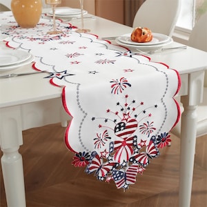 May include: White table runner with red, white, and blue embroidered fireworks, stars, and butterflies. The runner has a scalloped edge.