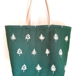 May include: A green tote bag with a repeating pattern of white pine trees. The bag has light tan leather handles and is made of a sturdy fabric. The bag is designed for carrying items.