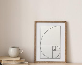 May include: A framed print of a black and white geometric design, featuring a spiral pattern. The print is in a light wood frame and is displayed on a light wood surface.