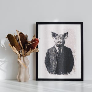 May include: A black and white framed print of a pig wearing a suit and tie. The pig is looking directly at the viewer. The print is hanging on a white wall next to a vase with dried flowers.