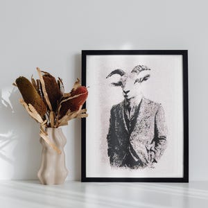 May include: A black and white framed print of a goat wearing a suit and tie. The print is on a white background and is hanging on a white wall. A vase with dried flowers is on a white table in front of the print.