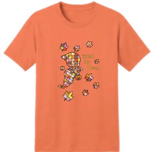 Könnte beinhalten: Ein orangefarbenes T-Shirt mit kurzen Ärmeln und einer Grafik eines Geistes mit buntem Karomuster. Der Geist hält einen kleinen Kürbis, umgeben von herbstlichen Blättern und dem gelben Schriftzug Trick Or Treat auf der Vorderseite.