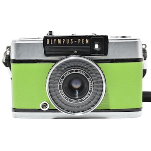 May include: A vintage Olympus Pen camera with a silver top and a bright green body. The camera lens is black and silver, with the text "OLYMPUS-PEN" above the lens. The camera has a black strap attached.