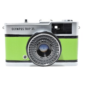 May include: An Olympus Trip 35 camera with a silver top and a bright green body. The camera lens is black and silver, with the text "Olympus Trip 35" printed on the front.