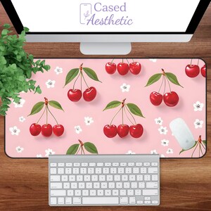 May include: A pink desk mat featuring a pattern of red cherries with green leaves and white flowers. The mat has a rectangular shape and is designed to be used with a computer mouse and keyboard. The text "Cased Aesthetic" is visible in the top left corner.