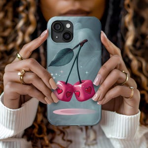 May include: A blue phone case with a cherry design. The cherries are red and have hearts on them. The background is a light blue with white stars.
