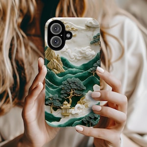May include: A phone case with a green, white, and gold design featuring a mountain landscape with clouds and a small building. The case has a raised design and a textured finish.