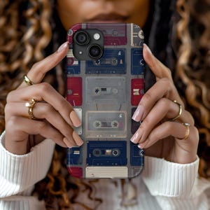 May include: A phone case with a retro design featuring a pattern of colorful cassette tapes. The case is made of durable plastic and has a clear back to show off the phone's design.