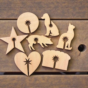 May include: Wooden cutouts in various shapes, including a star, heart, circle, dog, cat, pig, and bread. Each cutout features a starburst design. The objects are arranged on a wooden surface.