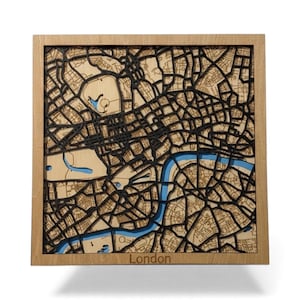 May include: A wooden map of London, laser-cut with intricate detail. The map highlights the city's layout, including streets, parks, and the River Thames in blue. The map is set in a natural wood frame, with the word "London" at the bottom.
