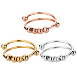 May include: Three spiral ear cuffs in rose gold, gold, and silver. Each cuff features a double spiral design with small, round beads. The rose gold and gold cuffs have warm tones, while the silver cuff has a cool, metallic sheen.