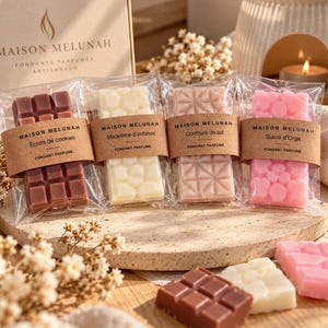 Peut inclure: Quatre fondants parfumés rectangulaires sous emballage plastique transparent, avec des étiquettes en papier kraft marquées Maison Melunah. Les barres sont marron, blanc, rose pâle et rose vif, avec des motifs en grille, alvéolés et cœurs.