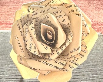 以下が含まれることがあります： 本から作られた手作りの紙のバラ。花びらは薄いクリーム色で、本からのテキストが見えます。ユニークな装飾品で、家の装飾やギフトに最適です。