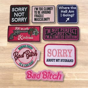 May include: A collection of embroidered patches with various phrases. The patches are in different shapes and colors, with text like "Sorry Not Sorry," "I'm Not Perfect," and "Bad Bitch." The patches are designed for clothing or accessories.