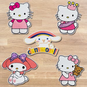 May include: Five embroidered patches featuring cartoon characters. Two patches depict Hello Kitty with pink bows and dresses. One patch shows Hello Kitty wearing a crown and a sash that says "Princess". Another patch shows a character with a rainbow and the word "cinnamoroll". The last patch shows a character with a bow and a teddy bear.