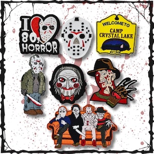 May include: A collection of embroidered patches featuring iconic horror movie characters and imagery. Includes patches with the text "I 80s HORROR", a heart-shaped mask, and "WELCOME TO CAMP CRYSTAL LAKE". Other patches depict characters like Freddy Krueger and Jason Voorhees.