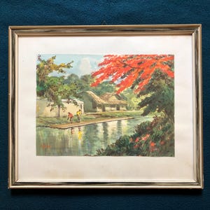 May include: Framed landscape painting depicting a tranquil scene with a body of water, a small house, and figures on a wooden structure. The artwork features vibrant colors, including red foliage and lush greenery, set against a light blue sky.