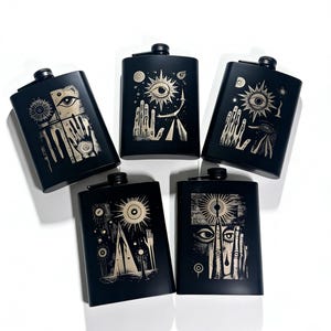 May include: Five black flasks with unique, cream-colored graphic designs. Each flask features a different surreal illustration, including eyes, hands, and celestial elements. The flasks have a matte finish and a small, black screw-on cap.