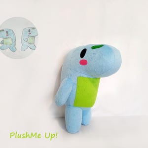 May include: A light blue plush toy with a green belly, black eye, and pink cheek. A small drawing of the plush toy is in a circle in the upper left corner. The text "PlushMe Up!" is in green at the bottom.