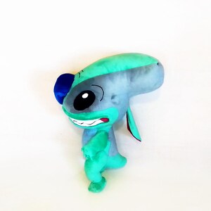 Peut inclure: Une peluche repr&eacute;sentant un personnage extraterrestre bleu et vert avec de grands yeux noirs, un large sourire et de grandes oreilles. Le jouet est principalement bleu et vert, avec des accents noirs et rouges. Le jouet est un personnage populaire d'un film.