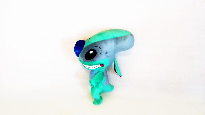 Peut inclure: Une peluche repr&eacute;sentant un personnage extraterrestre bleu et vert avec de grands yeux noirs, un large sourire et de grandes oreilles. Le jouet est principalement bleu et vert, avec des accents noirs et rouges. Le jouet est un personnage populaire d'un film.