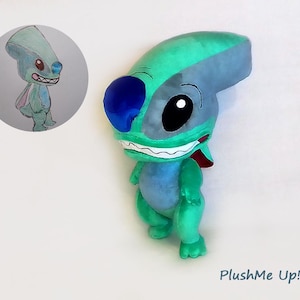 Peut inclure: Une peluche repr&eacute;sentant une cr&eacute;ature extraterrestre bleue et verte avec de grands yeux noirs et un large sourire. Un dessin du m&ecirc;me personnage est dans un cercle en haut &agrave; gauche. Le texte "PlushMe Up!" est en bas &agrave; droite.
