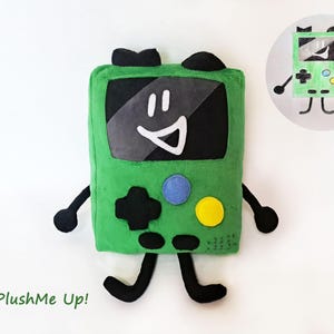 May include: A green plush toy resembling a retro handheld games console, featuring a smiling face, black limbs, and colourful buttons. The text "PlushMe Up!" is in the bottom left corner. A drawing of the toy is in the upper right corner.